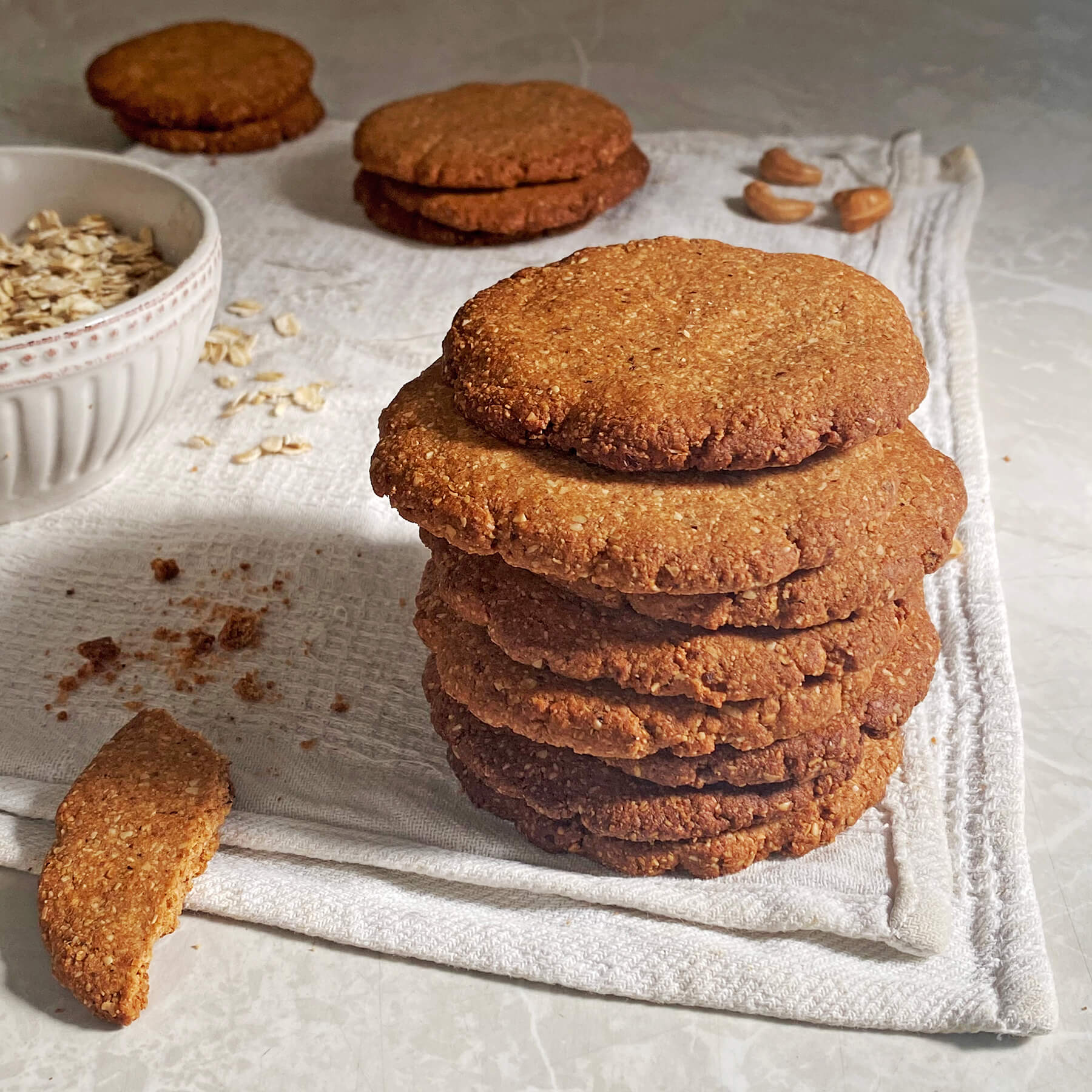 Pila de galletas, bowl con avena integral y castañas de cajú sobre un paño de cocina blanco