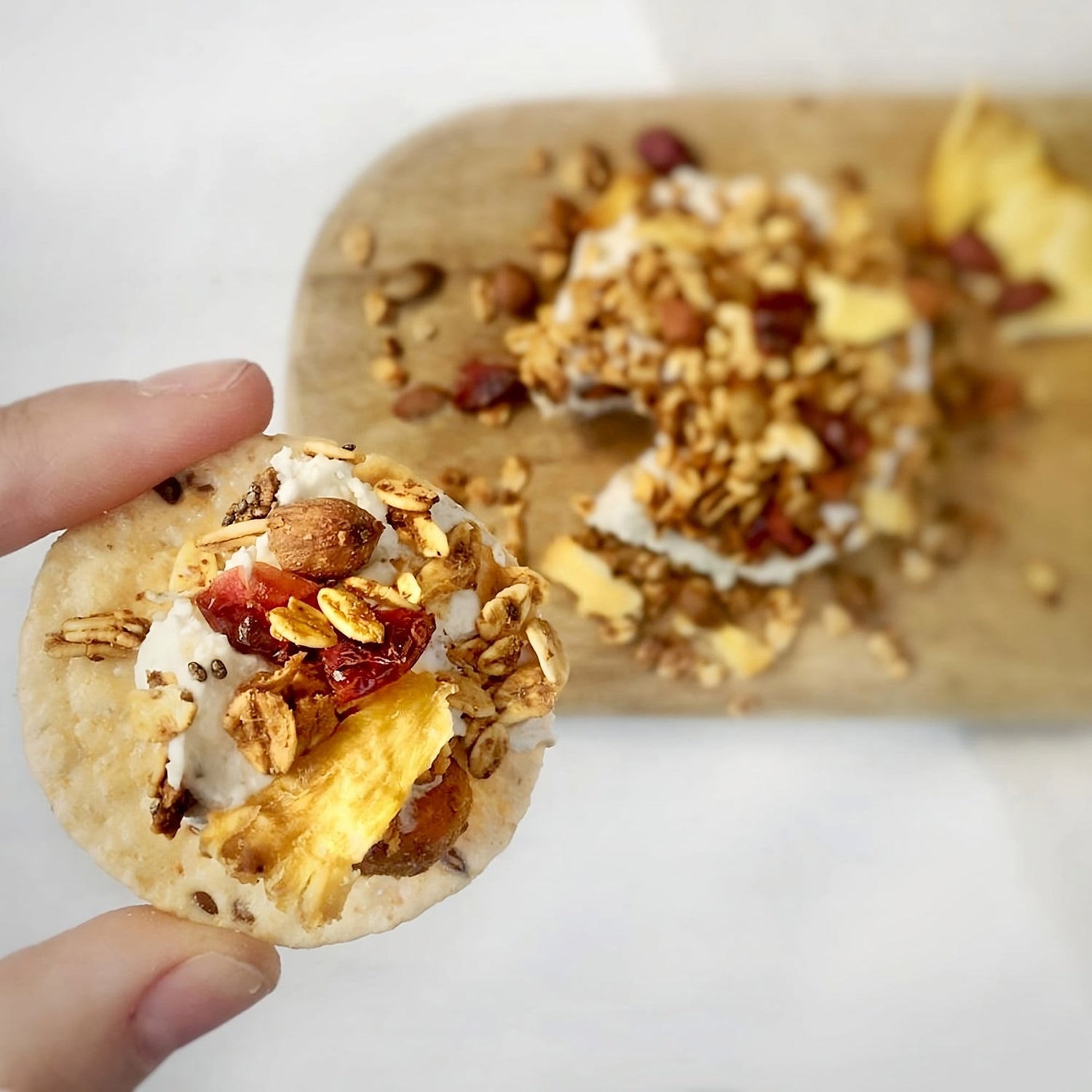 Dedos sosteniendo una galleta con queso untable y granola