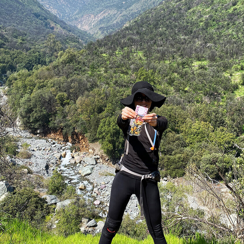 Mujer vestida de negro en las montañas sosteniendo un snack con las manos