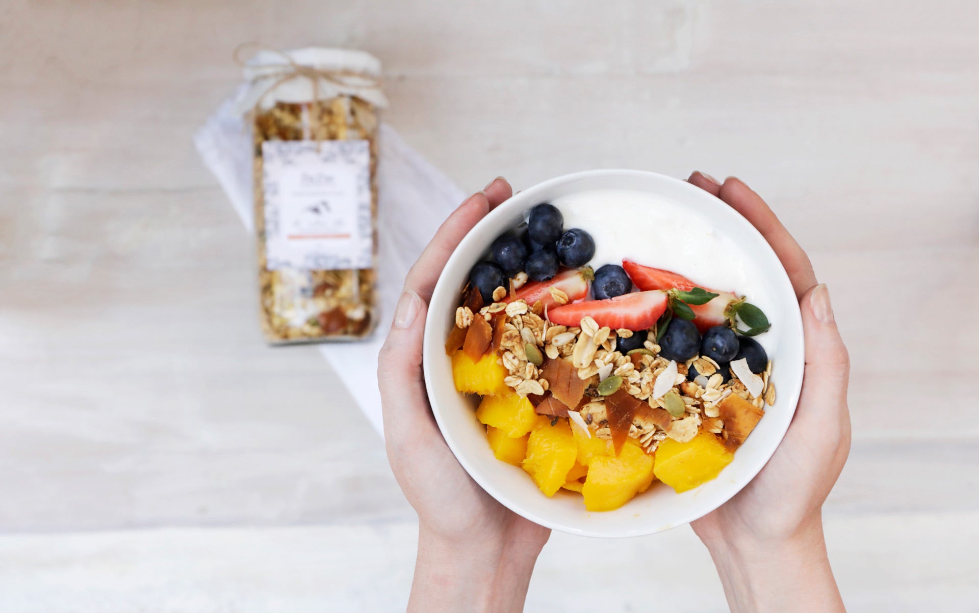 Manos sosteniendo un bowl con frutas yogur y granola