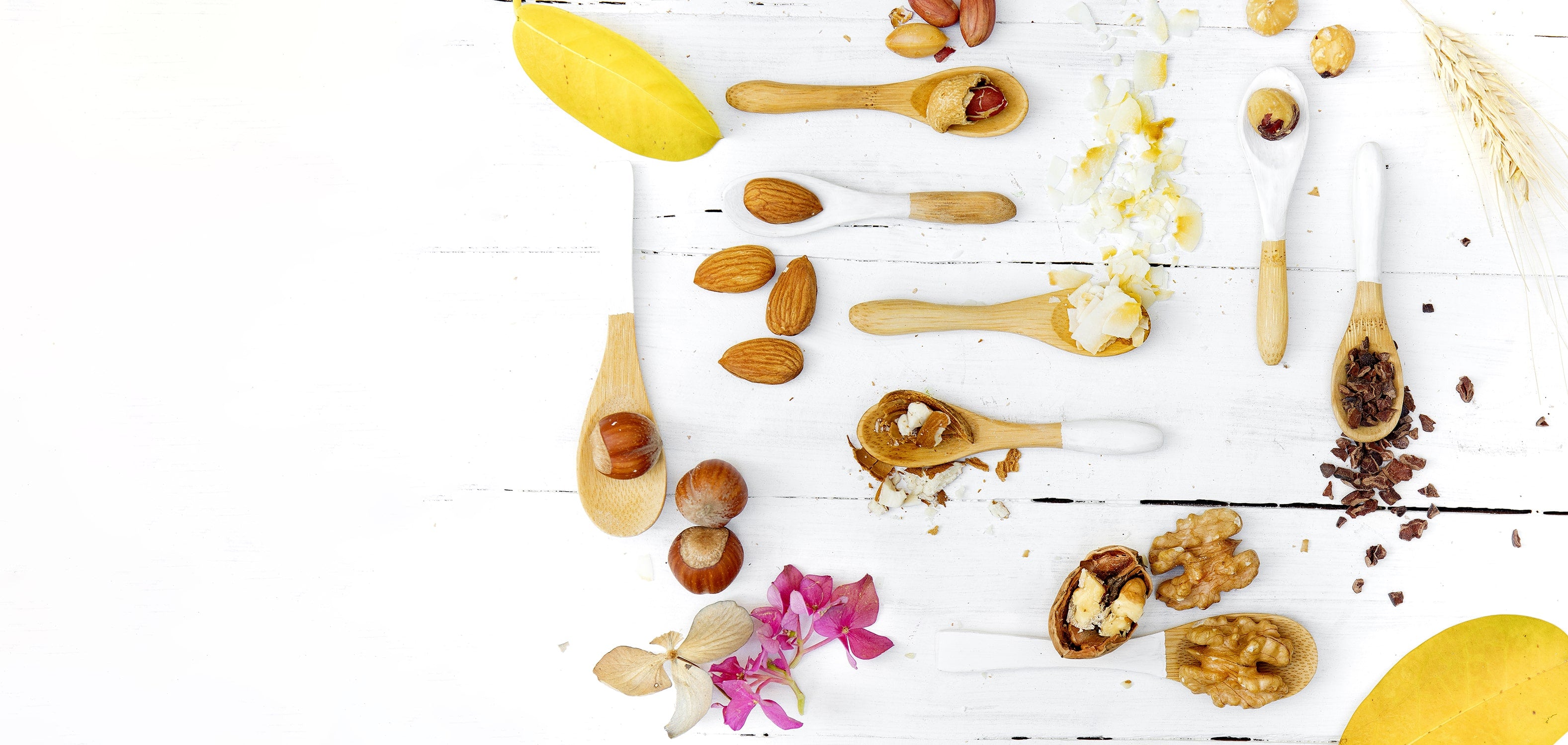 Cucharas de madera con frutos secos en fondo de madera blanca